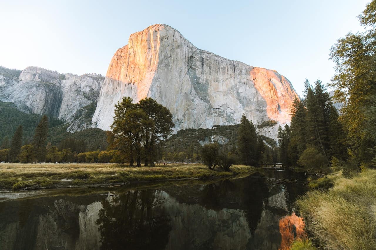 a mountain near a river, against a pale blue sky