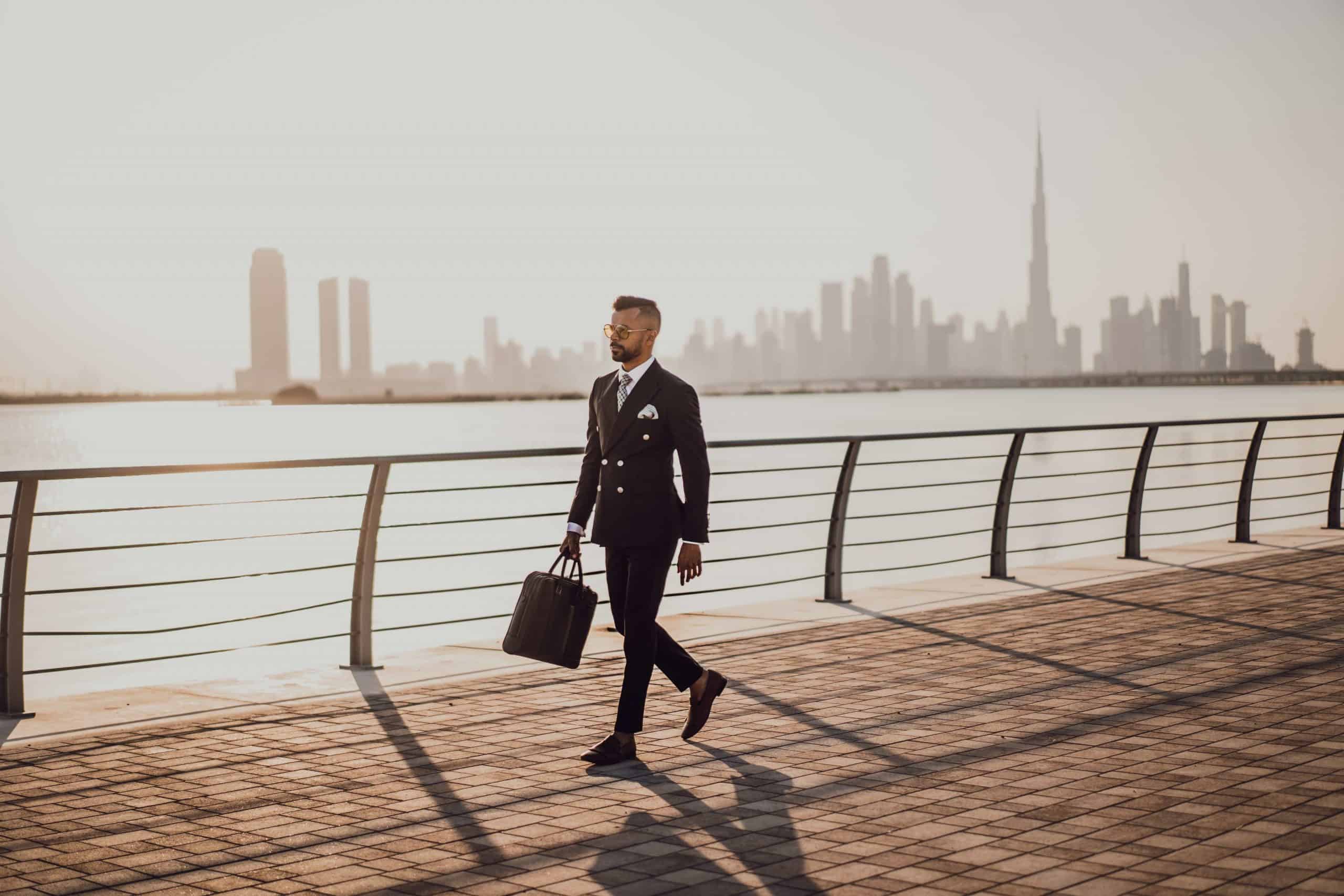 man in suit walking on the footpath with highrise buildings in the distance