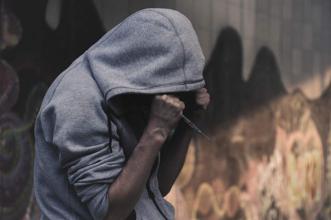 Man in grey hoodie holding a drug needle