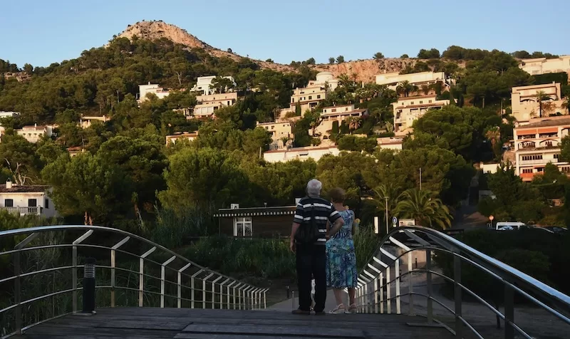 A couple takes in the view of a Mediterranean hillside community. From sun-drenched coasts to tranquil countryside towns, the dream of an affordable, fulfilling retirement abroad starts with finding the right place to call home.