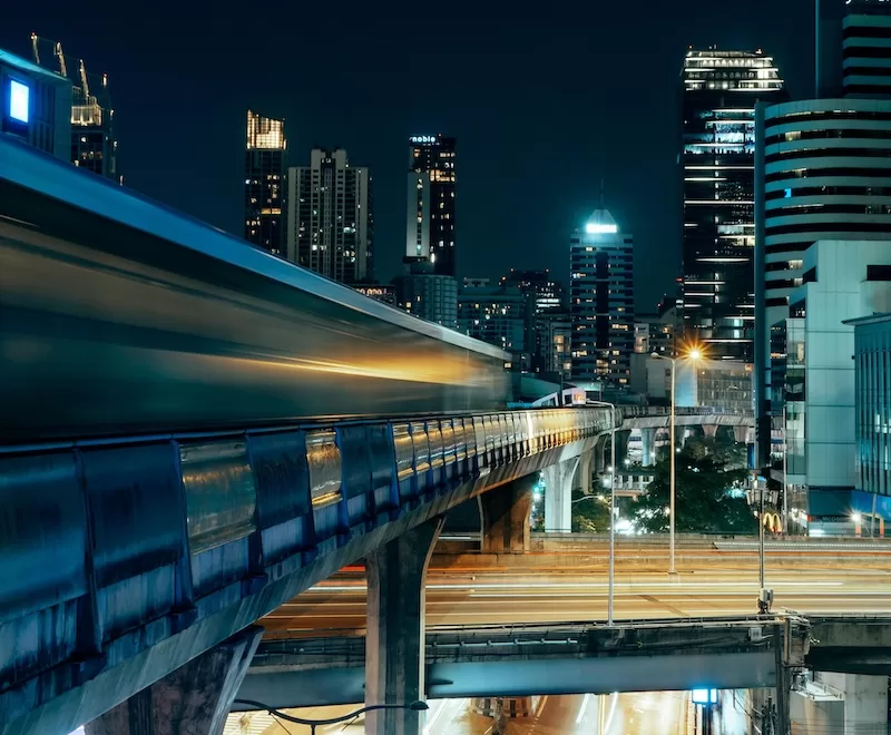 Bangkok’s BTS Skytrain gliding through the city at night. Proximity to transport hubs like this can significantly raise apartment rental prices.