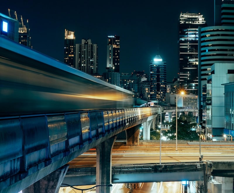 Bangkok’s BTS Skytrain gliding through the city at night. Proximity to transport hubs like this can significantly raise apartment rental prices.