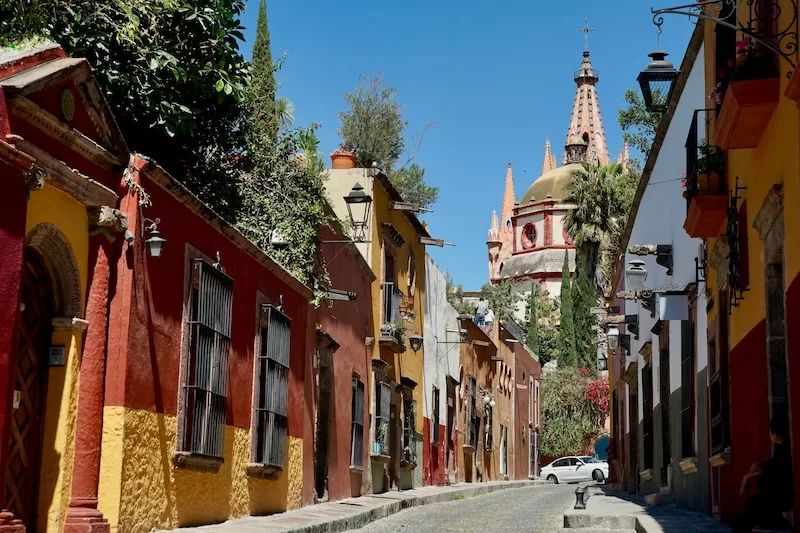 Colorful colonial facades line a cobblestone street in San Miguel de Allende, with the iconic Parroquia de San Miguel Arcángel rising in the background, a perfect snapshot of the town’s timeless charm.