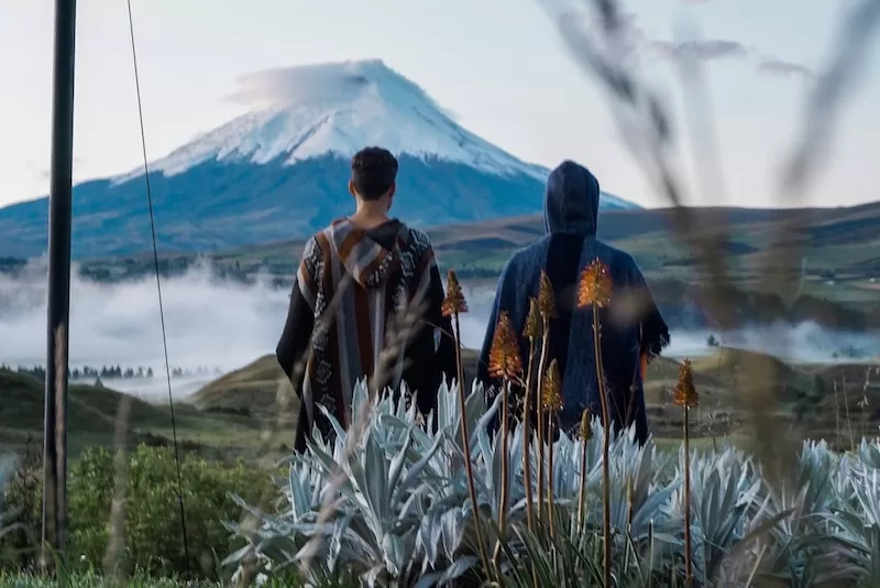 Two people stand before Cotopaxi Volcano, the same landscape that inspires Ecuador’s Tigua painters. In the highlands, art often begins with the earth: its colors, patterns, and rhythm mirrored in woven textiles and painted wood.