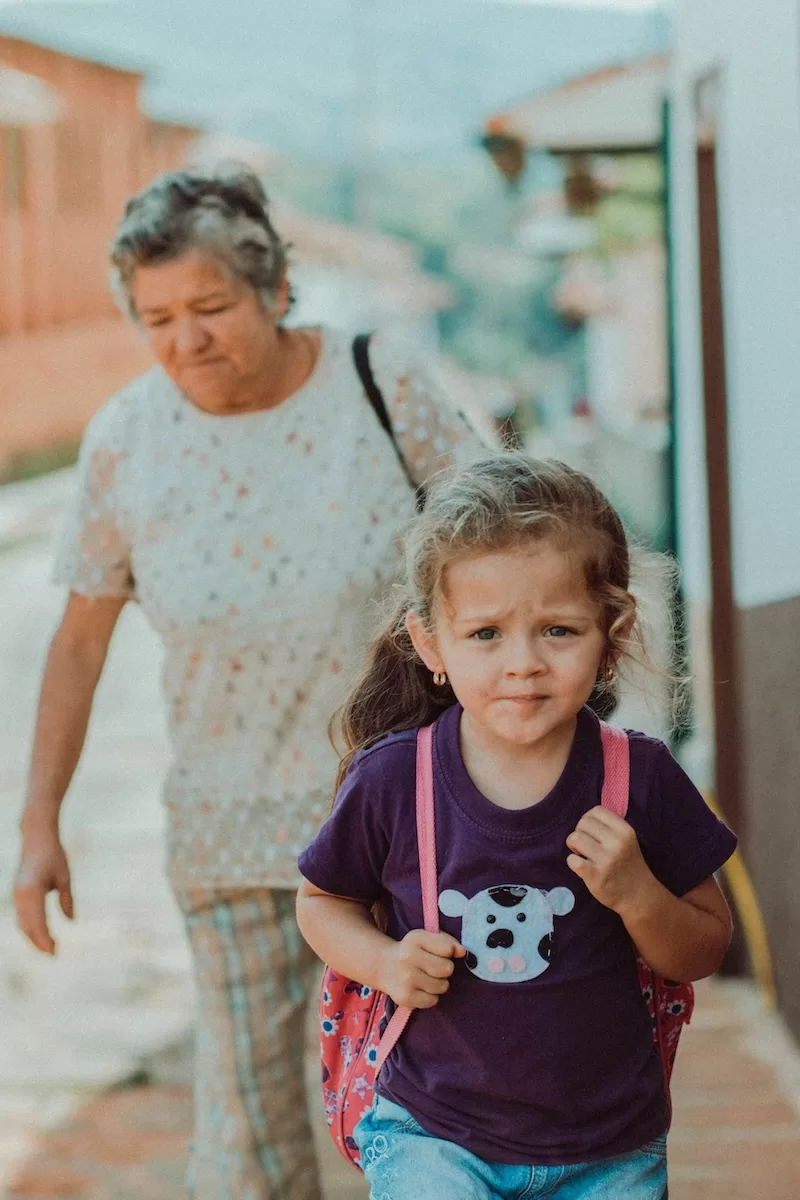 A grandmother walks her granddaughter through a quiet Colombian street, a glimpse of how generations care for and guide one another, passing down respect, patience, and love.