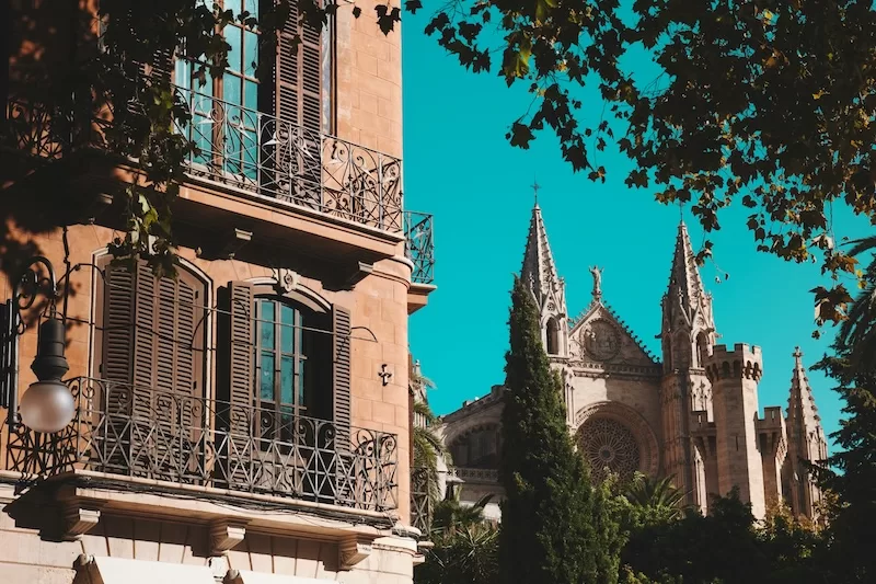 Palma’s Old Town holds layers of light and history. Balconies with weathered shutters, cathedral spires rising beyond the trees, and the feeling that every corner has a story waiting behind it.
