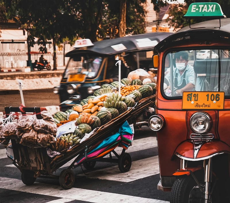 Transport and markets blend into one energetic scene. Tuk-tuks zip past fruit carts loaded with bananas, melons and vegetables, reminding newcomers that errands and commutes are never separate experiences.