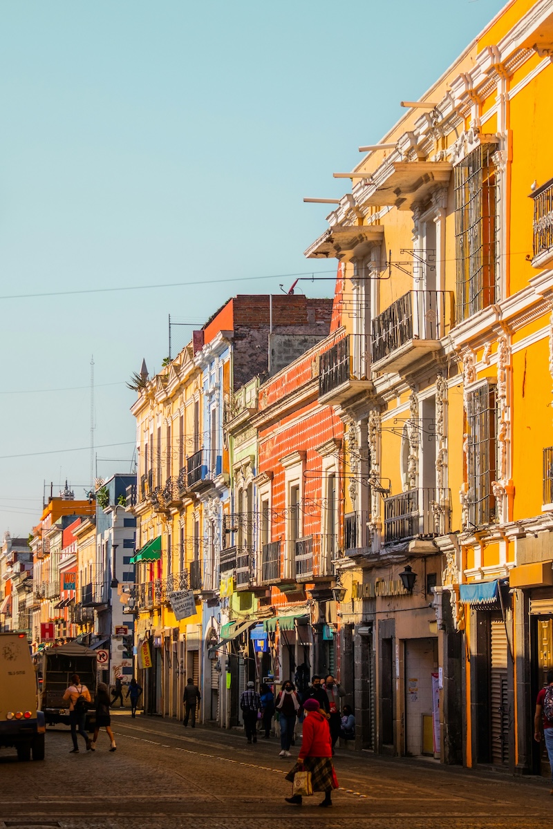 A sunlit stretch of Puebla’s colorful historic center, lined with balconies, cafés, and daily movement that give the city its lively but still affordable character.