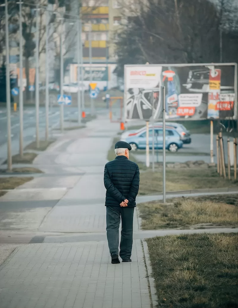 Elderly person walking on urban sidewalk with city buildings showing aging demographics and social challenges in developed countries like South Korea