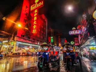 Vibrant Asian street at night with colorful neon signs, tuk-tuks, and illuminated storefronts, representing Bangkok's tourism challenges and urban cultural dynamics in overcrowded destinations