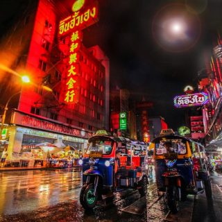 Vibrant Asian street at night with colorful neon signs, tuk-tuks, and illuminated storefronts, representing Bangkok's tourism challenges and urban cultural dynamics in overcrowded destinations