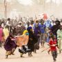 Large crowd of African families and children in colorful clothing gathered in dusty settlement, representing humanitarian crisis and displaced communities from regional conflicts and security crises