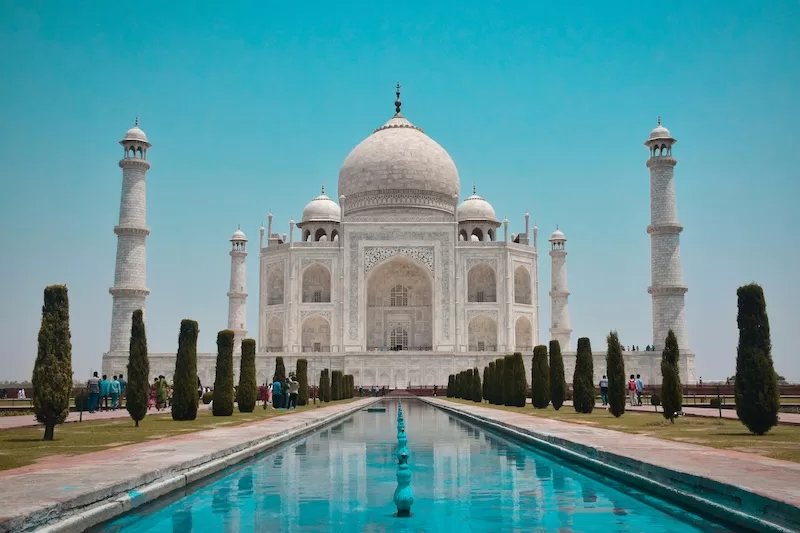 Taj Mahal monument with reflecting pool and manicured gardens under clear blue sky, representing India's cultural heritage and ongoing debate over historical interpretation and national identity