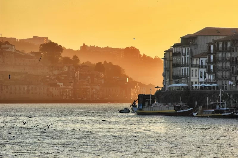Golden hour sunset over European waterfront city with historic buildings and boats, representing affordable living and financial benefits of building a life abroad