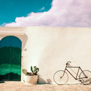 White Mediterranean-style building with green arched door and potted cactus plants, representing the lifestyle and independence offered by global property ownership