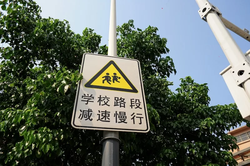 School zone warning sign with Chinese characters surrounded by green foliage, representing community safety and family considerations when establishing a second legal home
