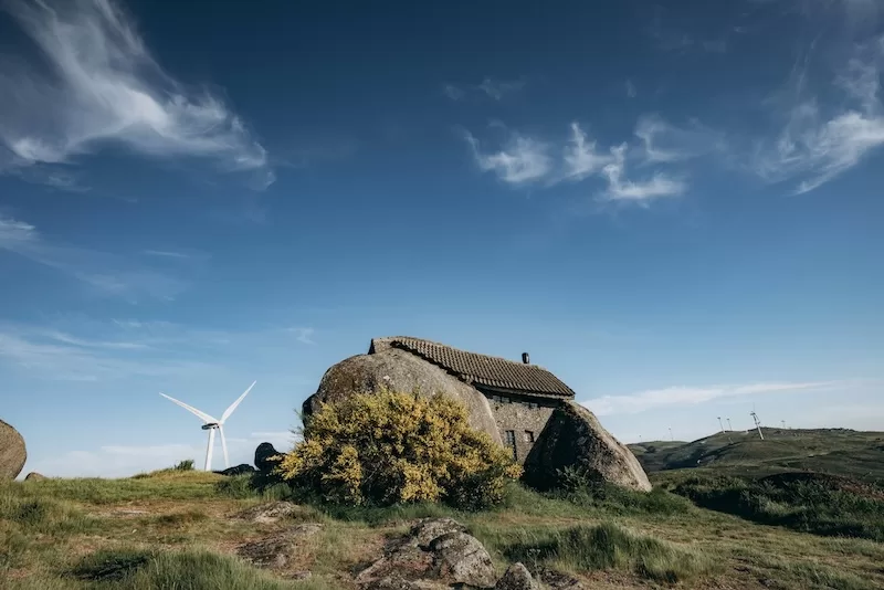 Remote stone house built on large boulder with wind turbine in background, representing sustainable living and independence through global property investment