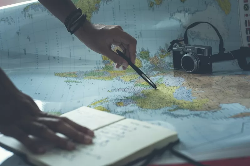 Traveler planning international relocation with world map, camera, and notebook, showing research and preparation for family move overseas