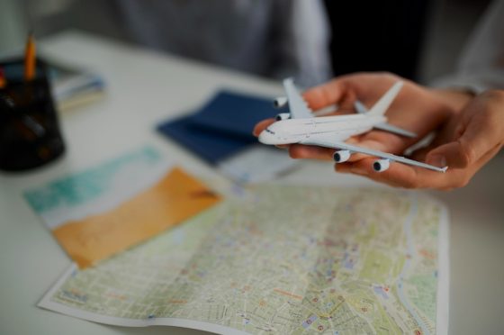 A person's hands hold a small white model airplane over a world map, symbolizing the careful planning and consideration required for expat relocation in a time of global economic uncertainty.