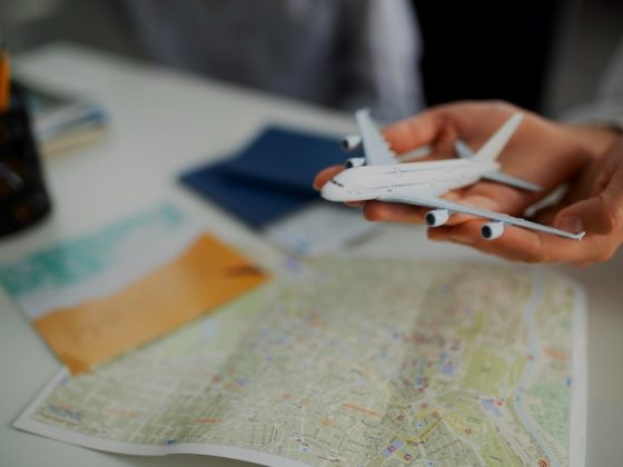 A person's hands hold a small white model airplane over a world map, symbolizing the careful planning and consideration required for expat relocation in a time of global economic uncertainty.