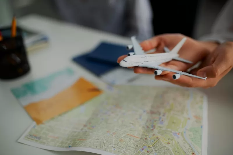 A person's hands hold a small white model airplane over a world map, symbolizing the careful planning and consideration required for expat relocation in a time of global economic uncertainty.