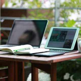 Remote worker with laptop and tablet at outdoor garden desk showing digital nomad lifestyle and location independence for global professionals seeking residency