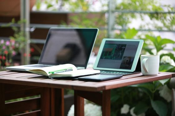 Remote worker with laptop and tablet at outdoor garden desk showing digital nomad lifestyle and location independence for global professionals seeking residency