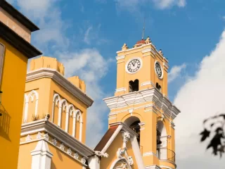 The bright yellow clock tower of the Xalapa Cathedral against a blue sky, representing the city's rich culture and history for potential expats.