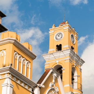 The bright yellow clock tower of the Xalapa Cathedral against a blue sky, representing the city's rich culture and history for potential expats.