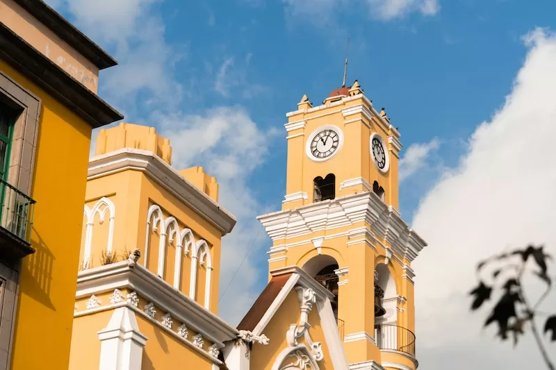 The bright yellow clock tower of the Xalapa Cathedral against a blue sky, representing the city's rich culture and history for potential expats.