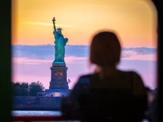 Woman viewing Statue of Liberty at sunset overlooking New York Harbor symbolizing U.S. immigration and global citizenship concerns during nationwide protests