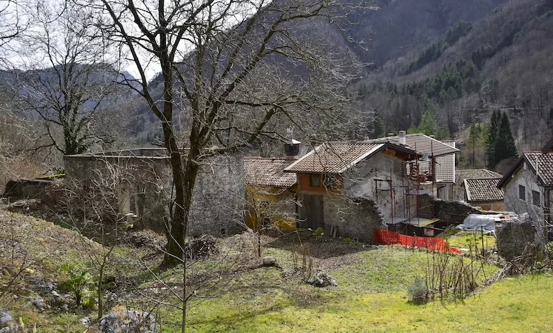 A cluster of old stone houses in a rural Italian village, some with scaffolding, illustrating the community-wide renovation efforts tied to the €1 house program.