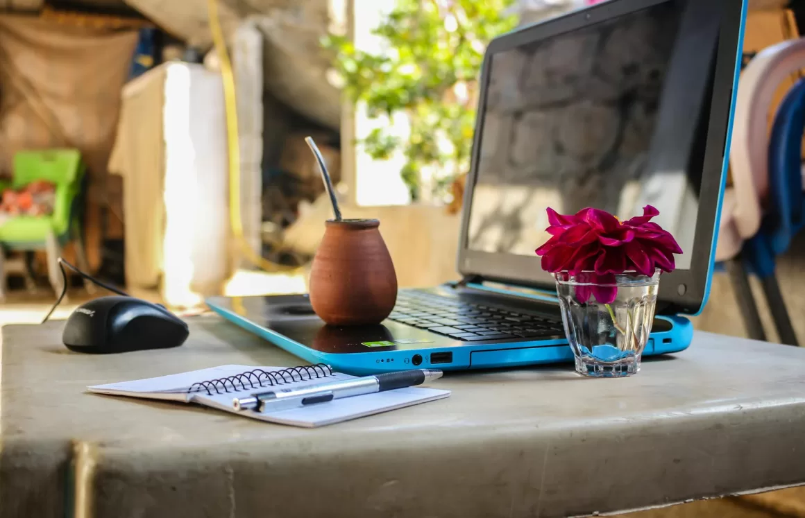 A digital nomad's remote work setup with a laptop, mate tea, and notebook, illustrating the blend of work and travel for long-term solo travelers.