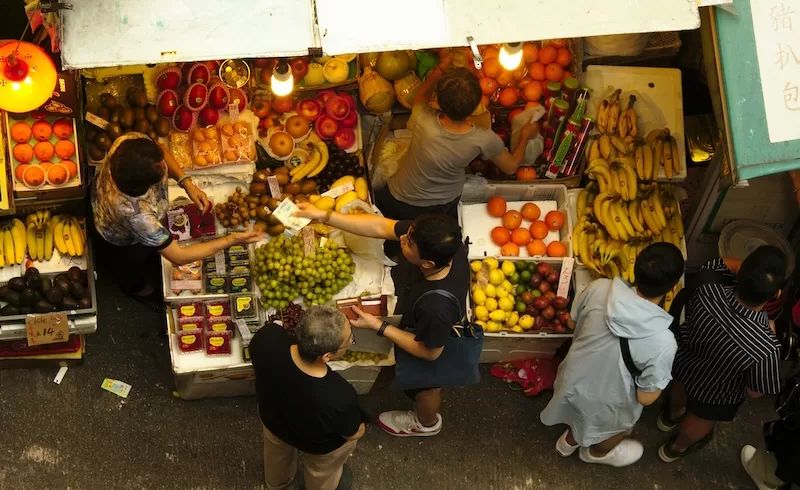 Overhead view of a bustling outdoor fruit market in Hong Kong, showcasing how to eat cheaply and support local economies while traveling sustainably on a budget.