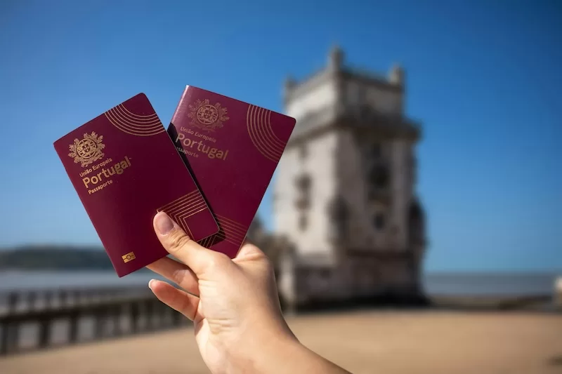 Portuguese passports held at historic tower showing path to Portuguese citizenship through digital nomad visa and residency programs for remote workers seeking EU citizenship