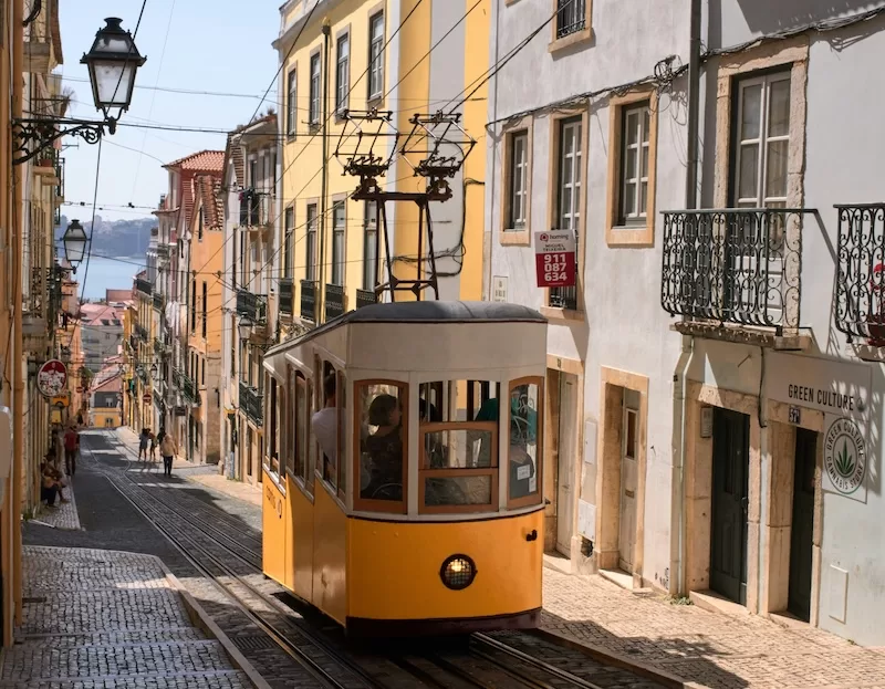 Classic yellow tram on a cobblestone street in Lisbon, Portugal, an example of using public transport for sustainable and budget-friendly European city travel.