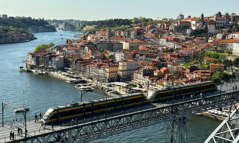 A modern yellow tram crosses the Dom Luís I Bridge in Porto, Portugal, a popular destination for bleisure travel, combining historic charm with modern infrastructure