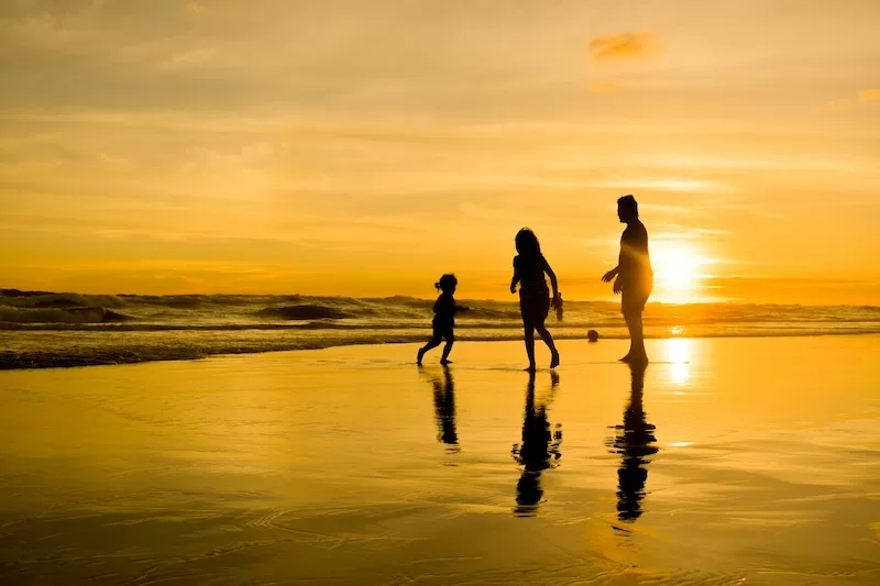 Family silhouettes at sunset beach enjoying quality time together, representing lifestyle improvements and family bonding from overseas relocation