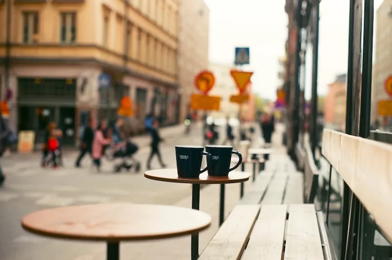 Two coffee mugs on a table at an outdoor cafe on a city street, representing the leisure and social aspects of a well-executed bleisure trip.