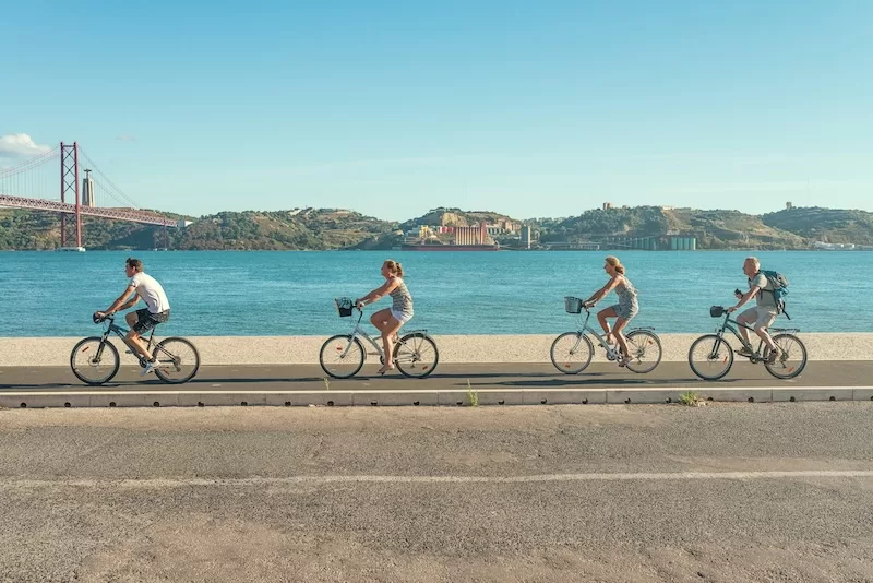 Family cycling along waterfront promenade with bridge view, showing active lifestyle and community integration for families relocating overseas