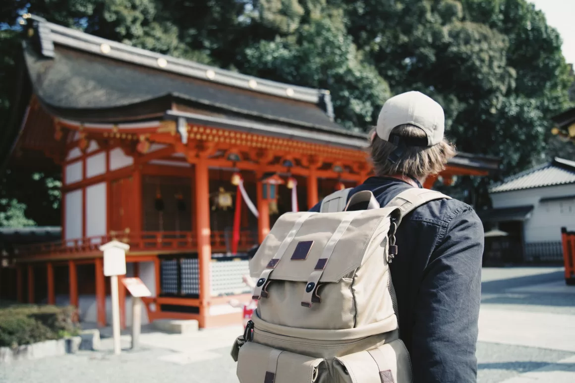 A solo traveler with a backpack admires a traditional red Japanese shrine, representing the deep cultural immersion possible when exploring solo travel destinations like Japan.