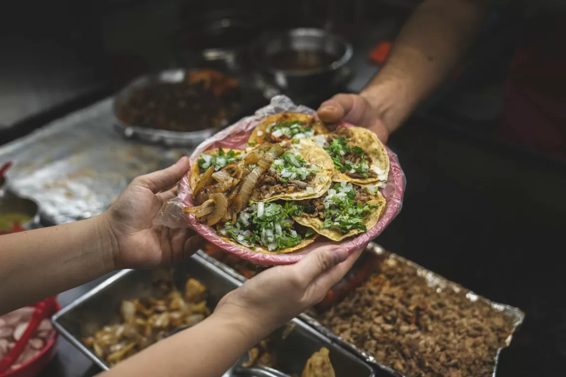 A person receives a plate of fresh street food tacos in Mexico, illustrating the authentic local experiences and culinary adventures that solo travel makes possible.