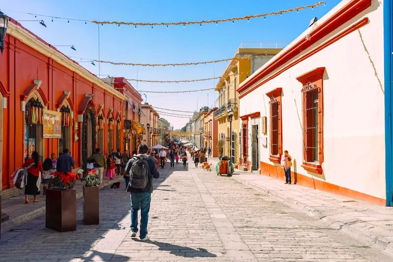 A man with a backpack walks down a colorful, cobblestone street in Oaxaca, Mexico, a perfect example of an immersive travel experience