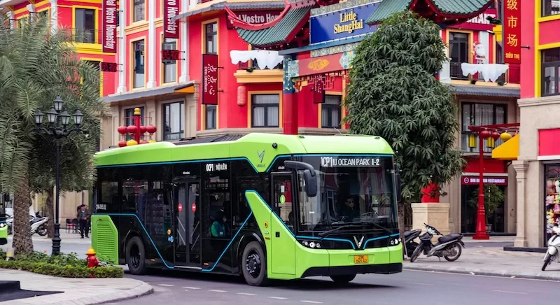 A modern, bright green electric city bus drives down a street, symbolizing the "Infrastructure as an Inflation Buffer" concept where reliable public transport helps expats avoid the hidden costs of car ownership.