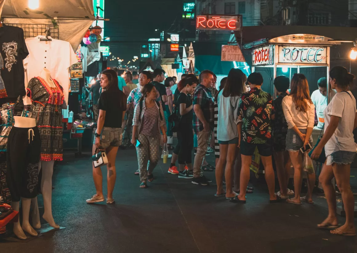 A bustling night market in Thailand with street food stalls and shoppers, showing the vibrant social atmosphere that solo travelers can experience in popular destinations.