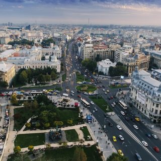 A red cable car descends from a lush green mountain, offering a breathtaking aerial view of the historic red-tiled roofs of Brasov, Romania, under a cloudy sky.