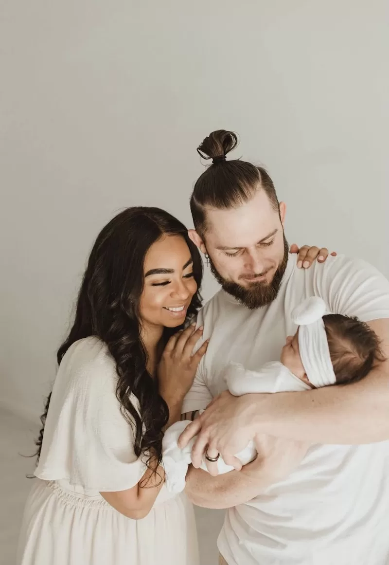 A tender black-and-white portrait of a mother and father looking lovingly at their newborn baby, capturing the early days of their journey as a family.