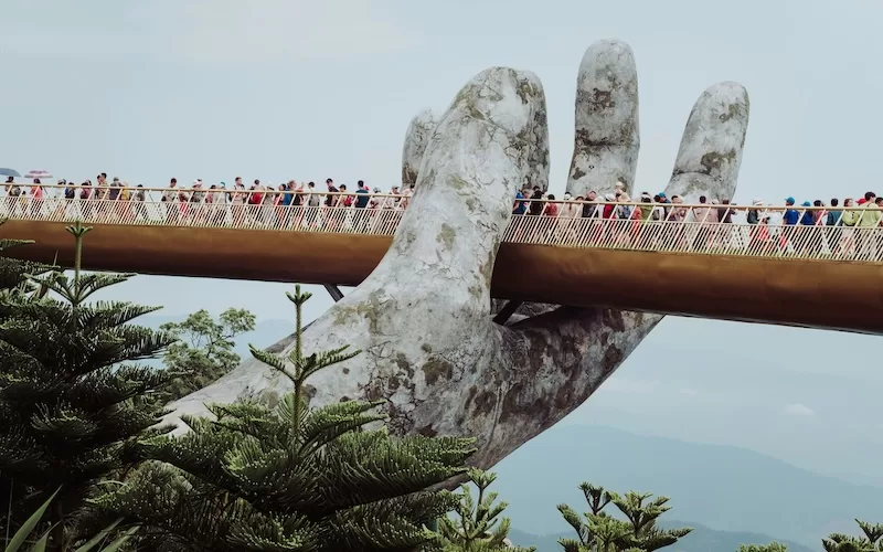 The Golden Bridge in Da Nang, Vietnam, held aloft by two giant stone hands, is bustling with tourists, offering panoramic views of the surrounding mountains and lush greenery.