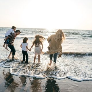 Family walking together along the beach shoreline with waves and sunset light behind them.