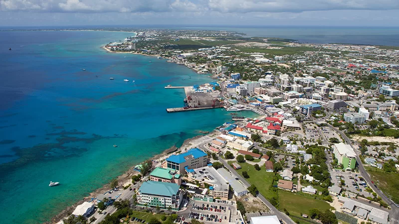 An aerial coastal view showing turquoise ocean water, white sandy beaches, colorful buildings, green vegetation, and a bustling seaside resort town